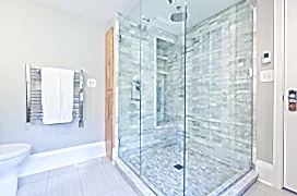 Contemporary interior bathroom design with glass enclosed shower stall with Cararra marble tiles. Duo shower heads with rain shower and conventional shower head. Heated towel rack hanger.