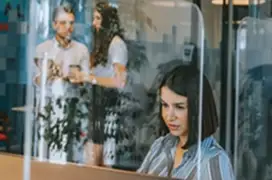 Young happy business woman working at her desk, smiling behind plexiglass panels between cubicle screen partition