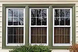 Three new replacement windows with green trim on front of house.