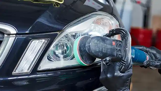 Mechanic worker burnish and polishing automobile car headlight by buffing grinding machine in garage workshop.