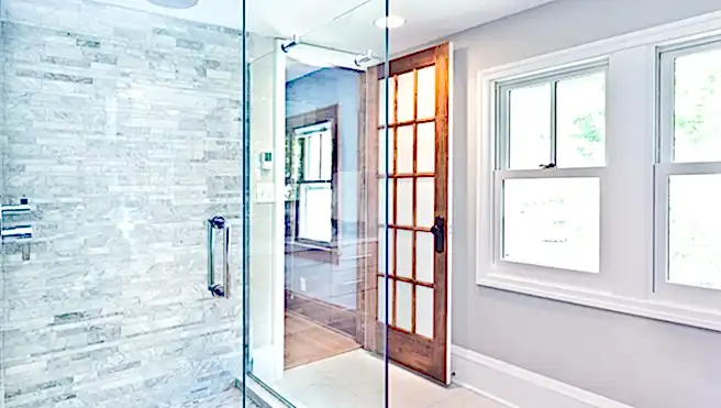 A modern design bathroom featuring a glass enclosed shower stall with marble tiles and rain shower fixture.