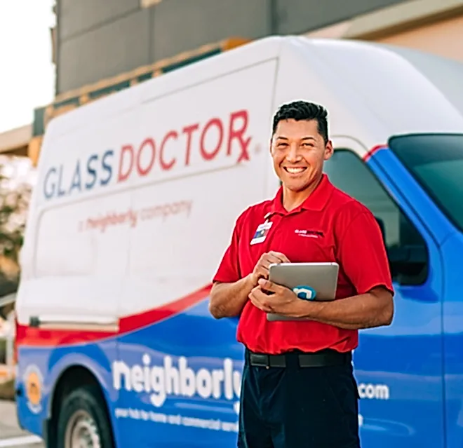 Glass Doctor professional holding a tablet while standing in front of a company van.